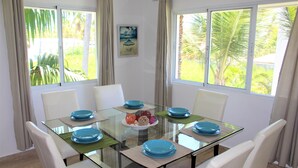 A dining area with a glass table surrounded by white chairs, a central decorative bowl, and a view of greenery outside. - CORTE SEA Luxury apartment in the heart of Bavaro (Punta Cana)