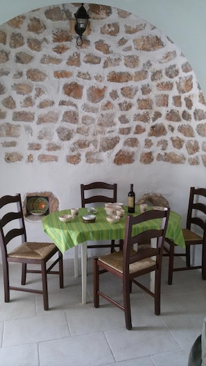 Zona pranzo con parete in pietra, tavolo con tovaglia verde e sedie di legno.