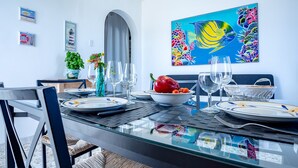 A dining area with a glass table, chairs, and a painting of a fish.