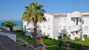 Un bâtiment blanc doté d’un balcon incurvé, de palmiers et offrant une vue dégagée sur la mer.