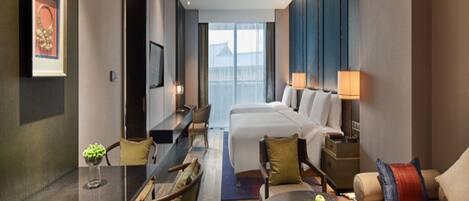 A hotel room with a bed, a desk, a chair, a round table with a fruit plate, and a TV on the wall.