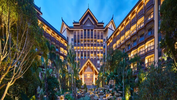 Un hotel de estilo arquitectónico tradicional, con un edificio central de varios pisos y balcones, rodeado de abundante vegetación y un jardín ajardinado con una pequeña cascada.