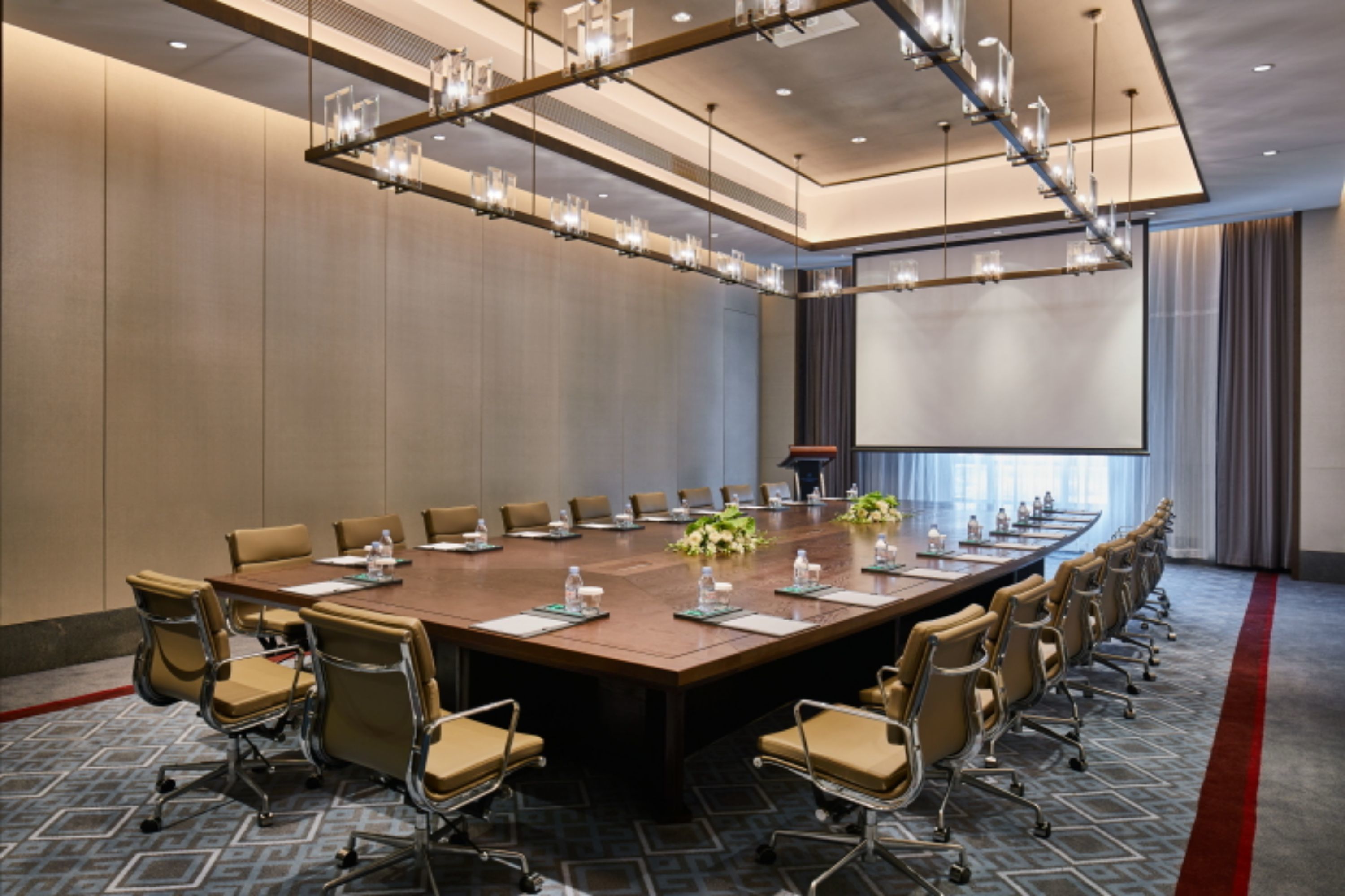 A conference room with a long table, multiple chairs, and a projector screen.