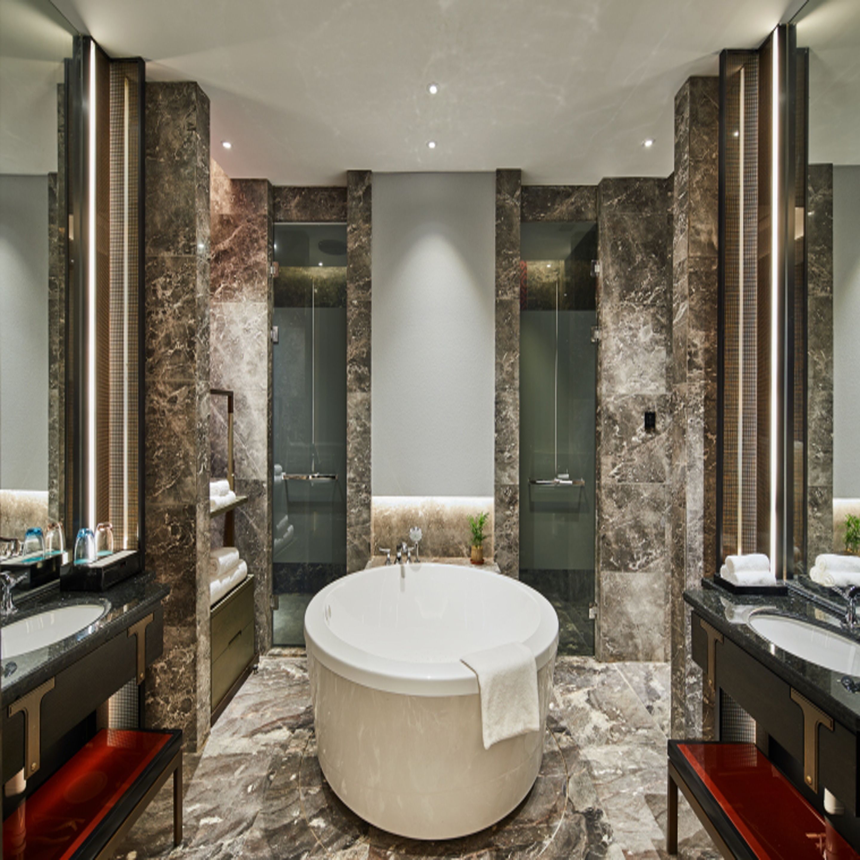 A modern bathroom with a large oval bathtub, two sinks, and a glass-enclosed shower.