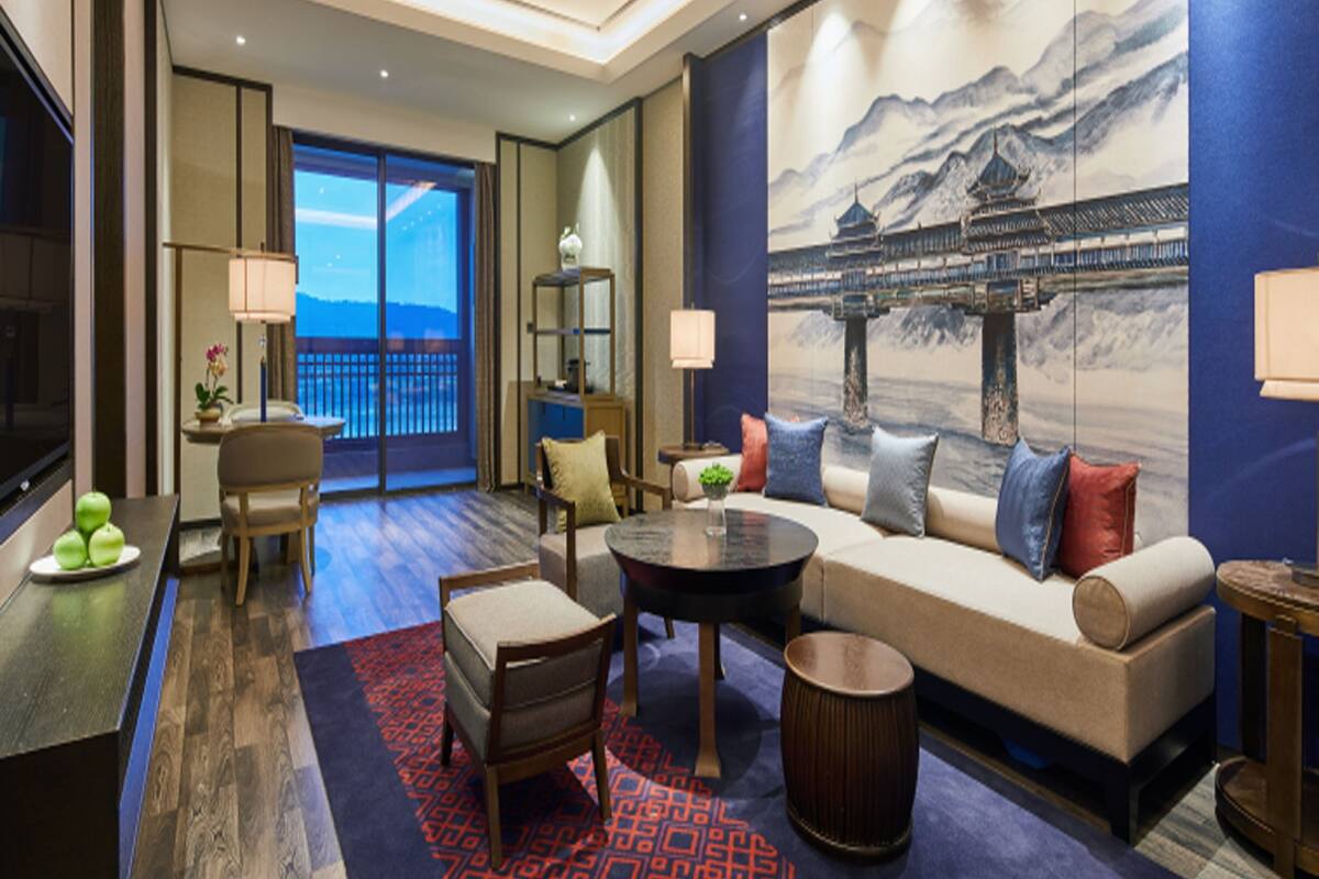Habitación de hotel moderna con un ventanal grande, un sofá, una mesita de centro y un cuadro de un puente tradicional.