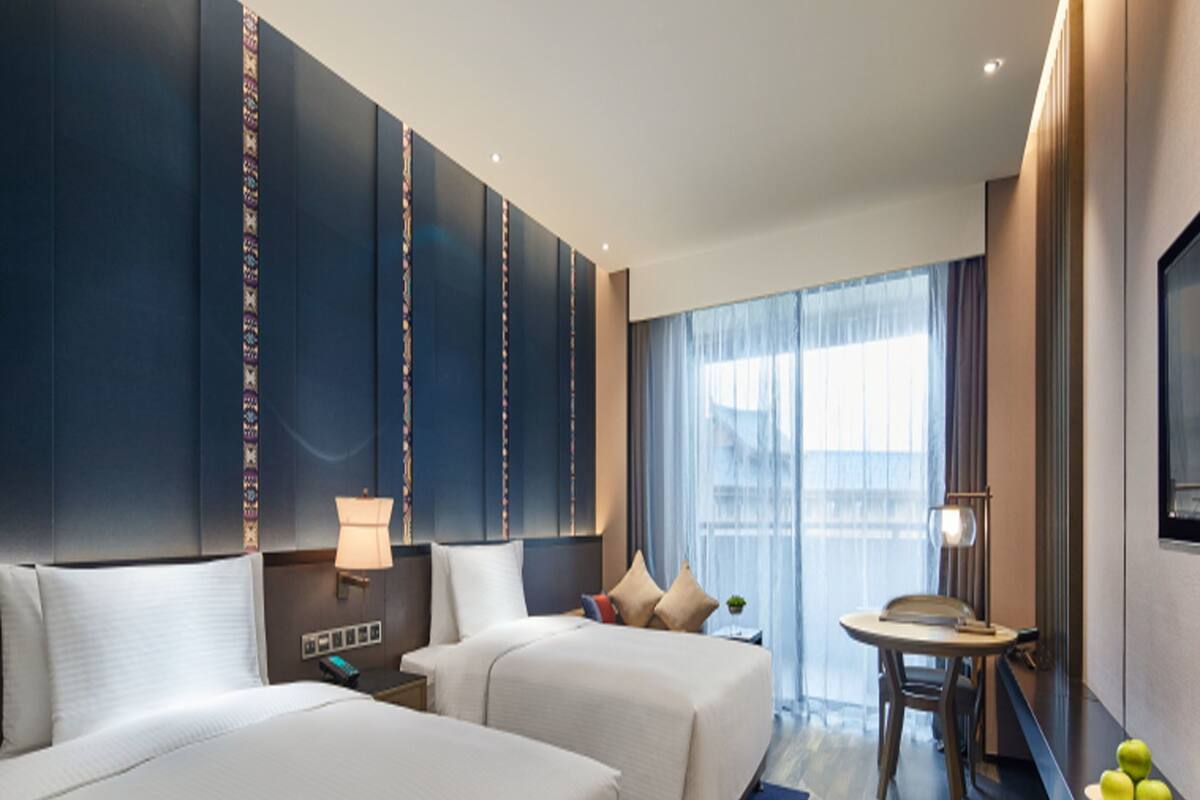 Habitación de hotel con dos camas, un escritorio, una silla, una lámpara y vistas a la ciudad.