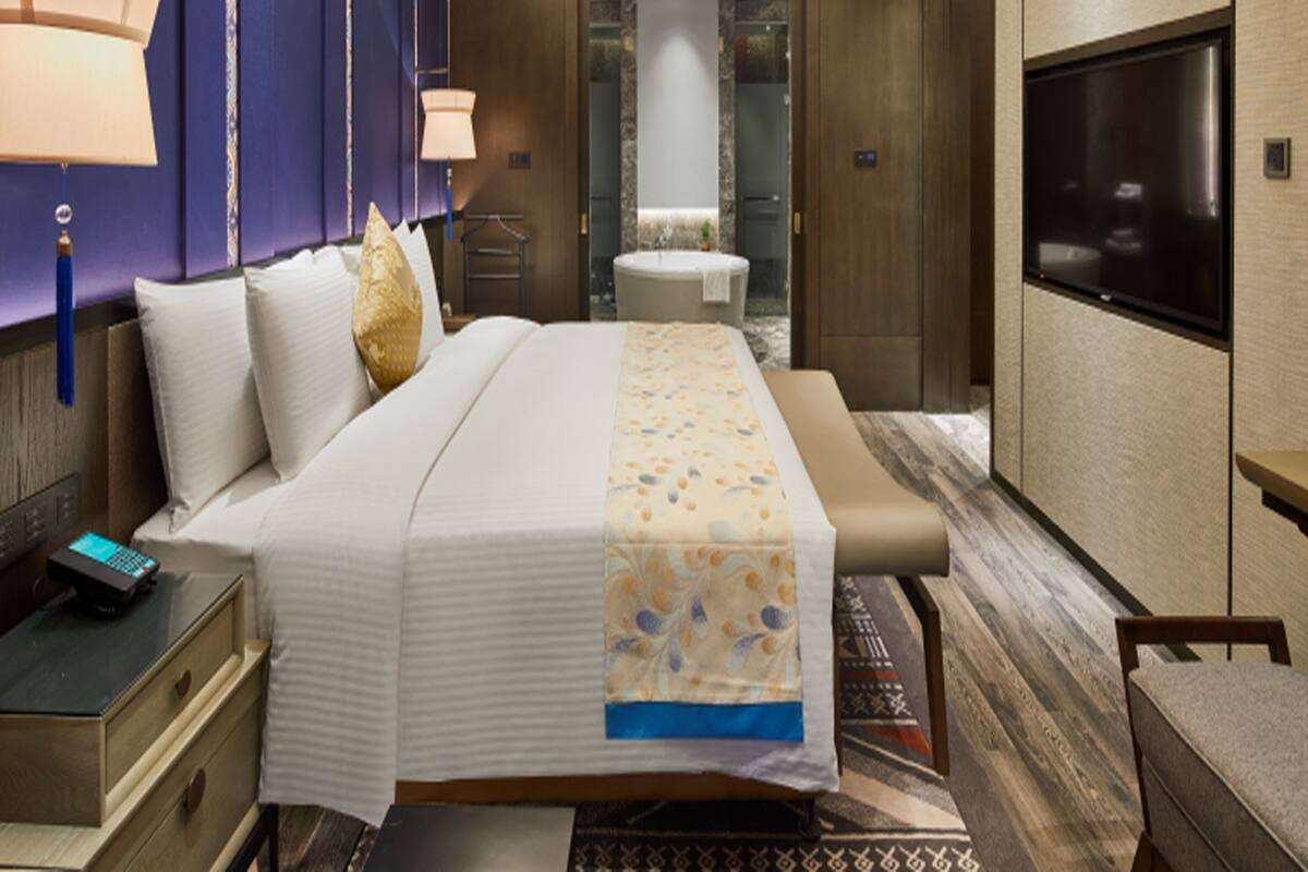 Habitación de hotel moderna con una cama grande, lámparas de noche, televisor y un baño visible a través de una puerta abierta.