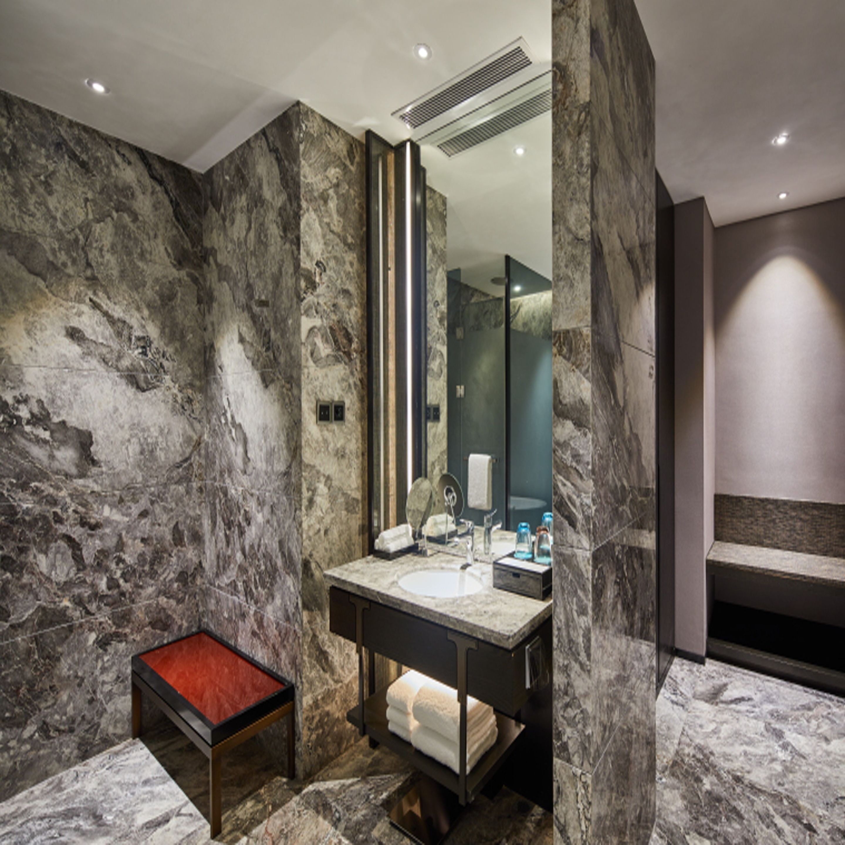 Ein modernes Badezimmer mit Marmorwand, Waschbecken mit Spiegel und Sitzbank.