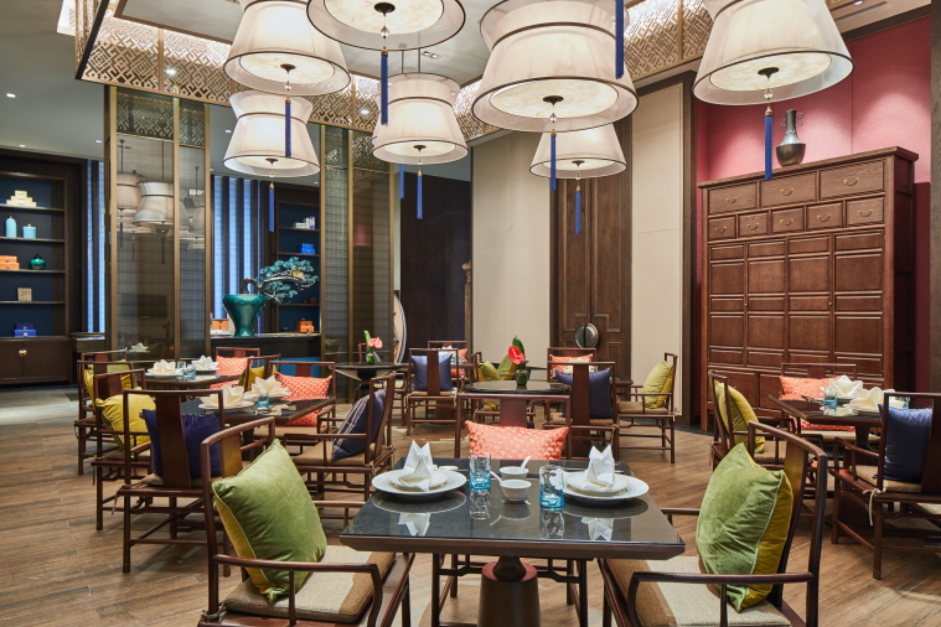 A dining area with multiple tables and chairs, large hanging lamps, and a decorative cabinet.