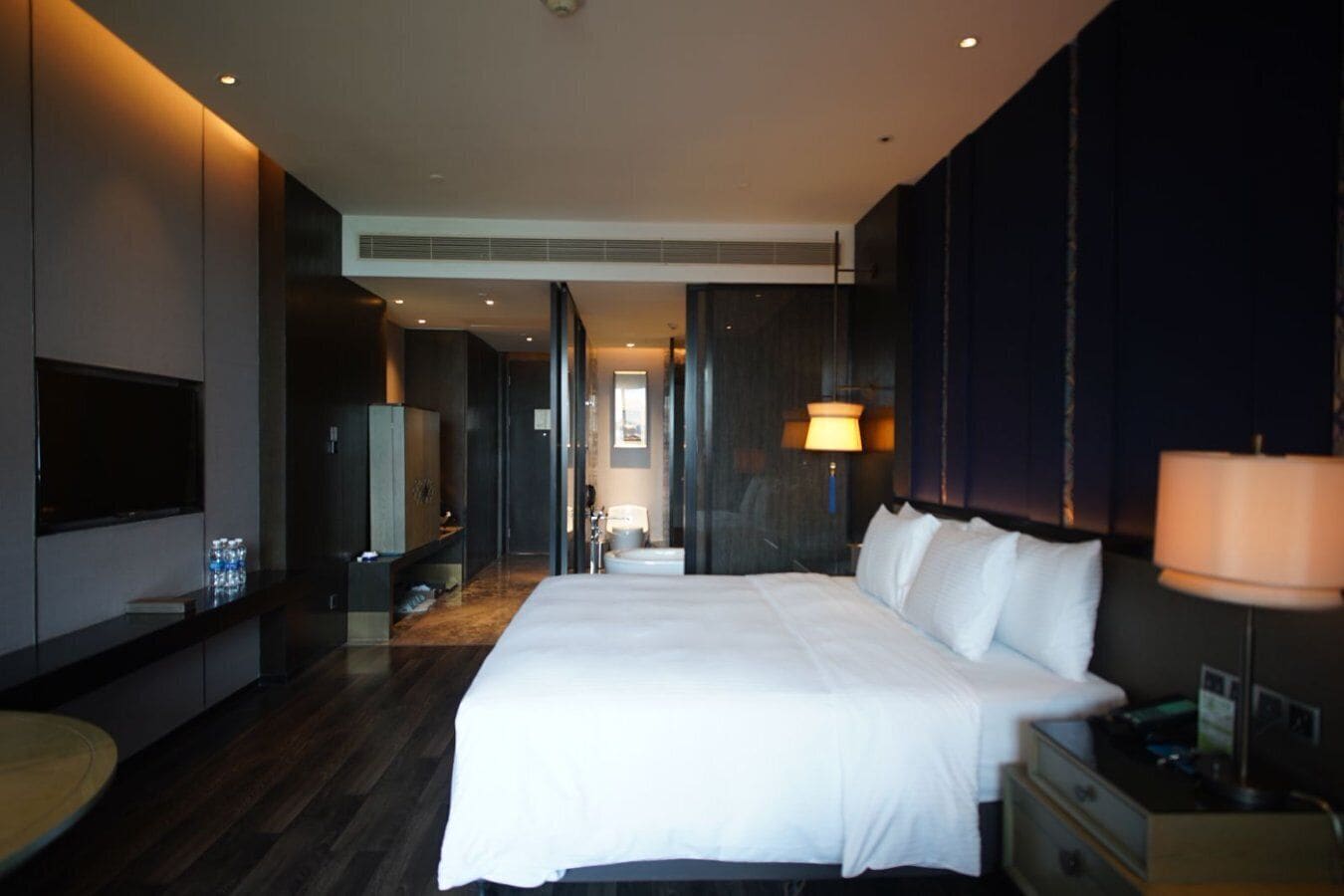 Une chambre d’hôtel moderne dotée d’un grand lit, d’une télévision, d’un minibar et d’une salle de bain visible à travers une porte ouverte.