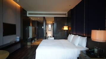 Une chambre d’hôtel moderne dotée d’un grand lit, d’une télévision, d’un minibar et d’une salle de bain visible à travers une porte ouverte.