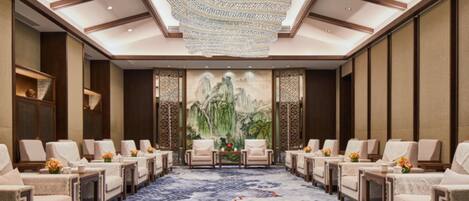 A spacious room with a patterned carpet, multiple seating areas, and a large wall painting.