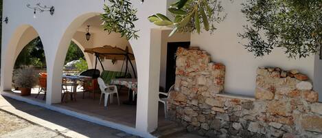 A covered outdoor seating area with a table and chairs, stone walls, and a pergola.
