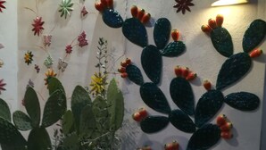 Een cactuspunt in een witte pot en een decoratieve muur met cactussen en bloemen.
