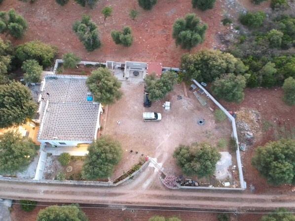 An aerial view of a property with a tiled-roof building, a gravel driveway, and surrounding trees.