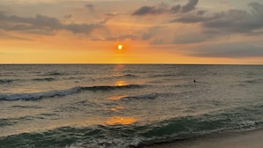 A sunset over the ocean with waves and a person swimming. - The Palms Resort & Bar (San Narciso)