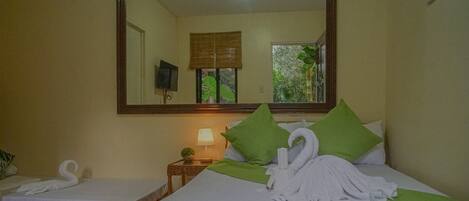 Habitación de hotel con dos camas, un espejo grande, una mesita con lámpara y vistas a zonas verdes.
