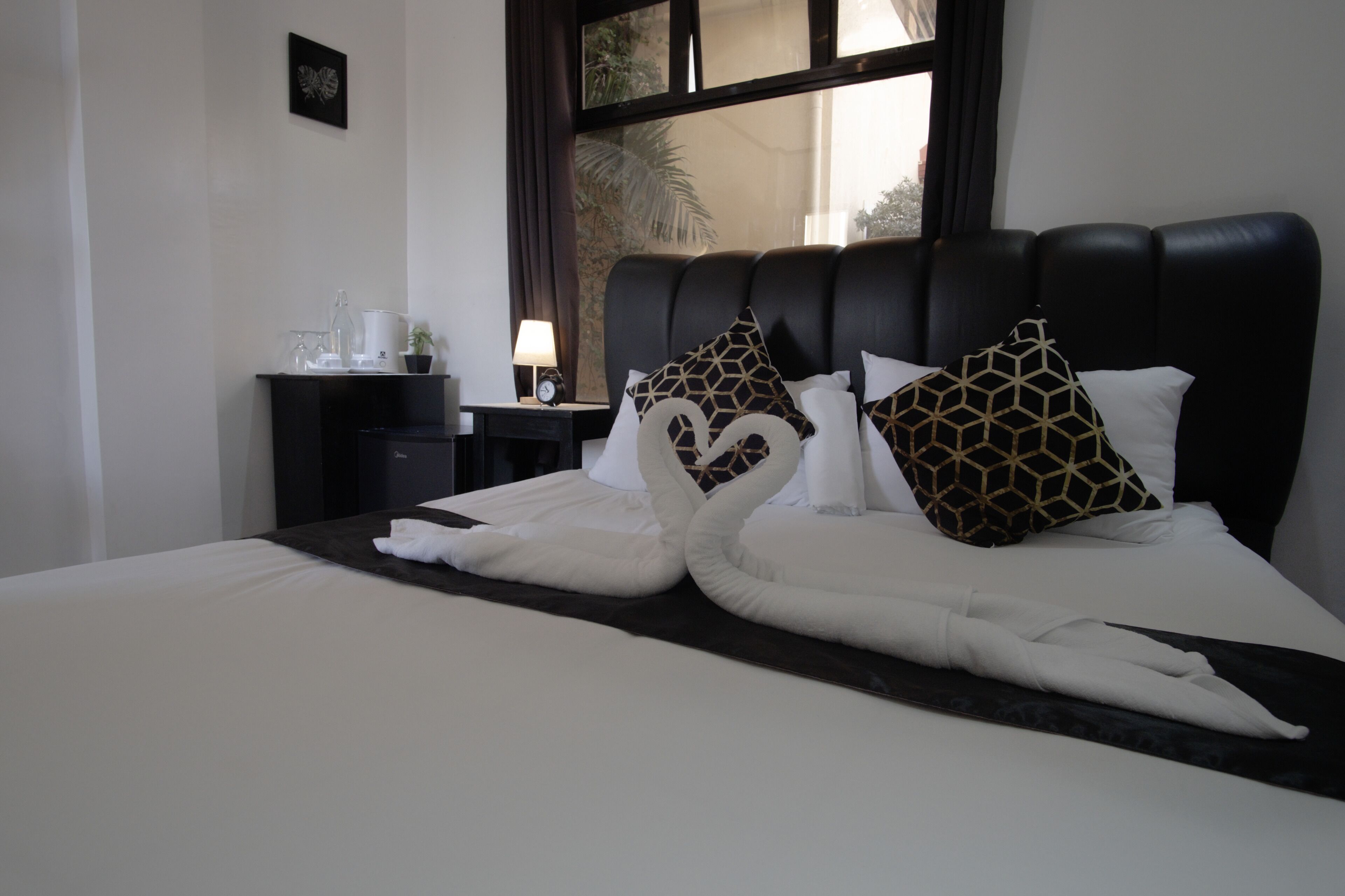 A hotel room with a bed featuring a swan-shaped bed runner, a black headboard, and a nightstand with a lamp and a clock.