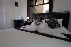 A hotel room with a bed featuring a swan-shaped bed runner, a black headboard, and a nightstand with a lamp and a clock. - The Palms Resort & Bar (San Narciso)