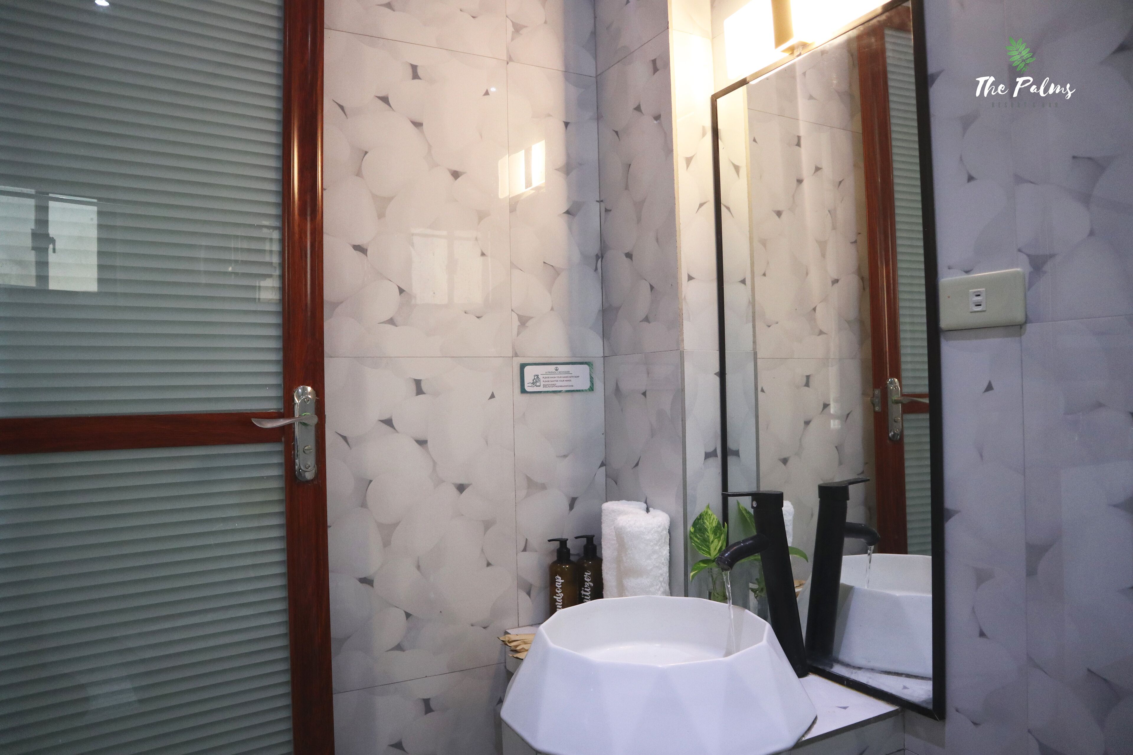 Ein Badezimmer mit einem weißen Waschbecken, einem großen Spiegel und einem Handtuchspender.