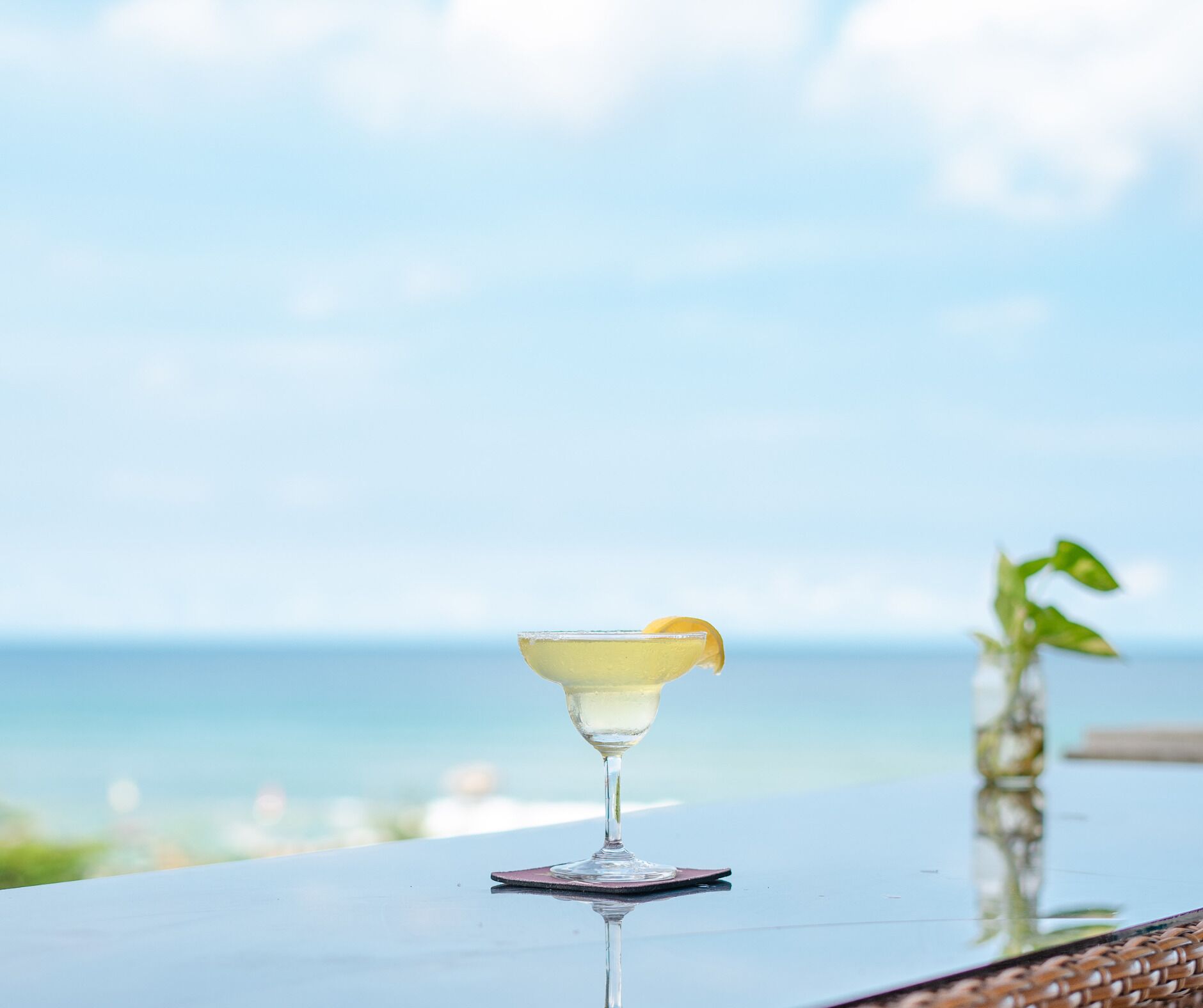 A cocktail glass with a lemon garnish on a table by the ocean.