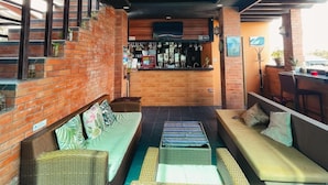 A bar area with a wooden ceiling, brick walls, and a seating area with wicker furniture. - The Palms Resort & Bar (San Narciso)