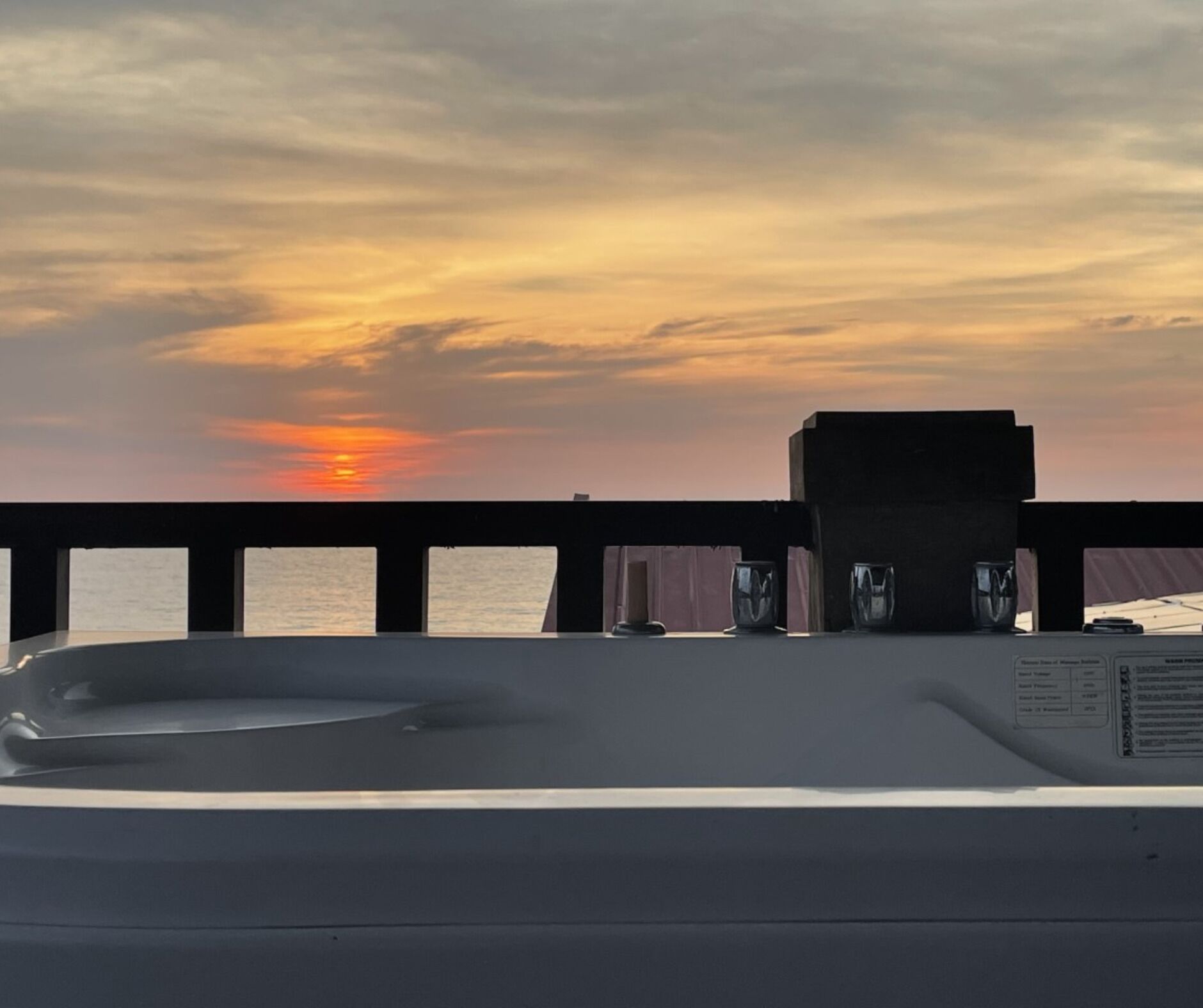 A sunset view from a balcony with a railing, a small seating area, and a view of the sea.