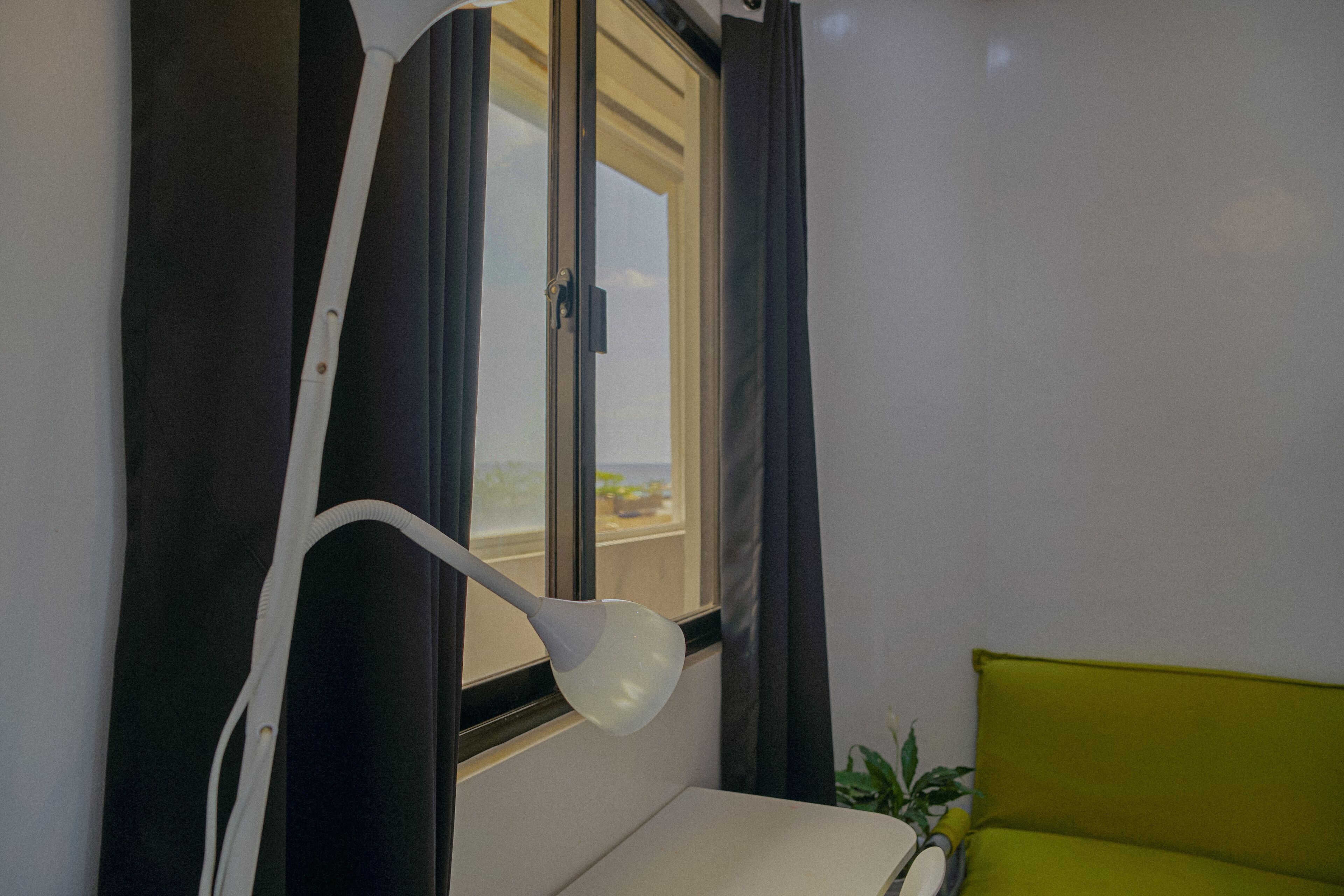 Et værelse med et vindue, en hvid lampe, en grøn sofa og en plante.