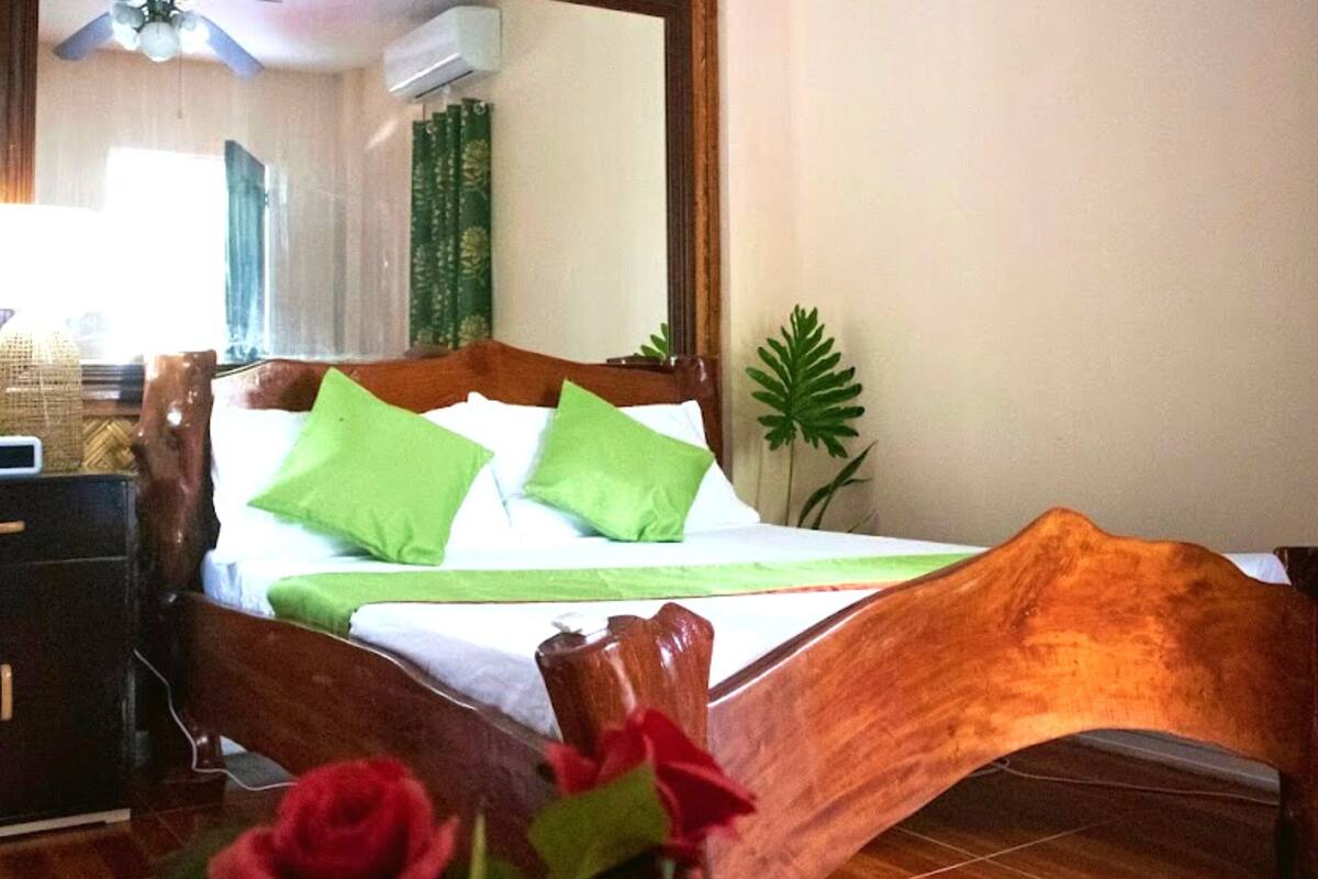 Una cama de madera con almohadas verdes, una mesita de noche con una lámpara y un espejo en la pared.