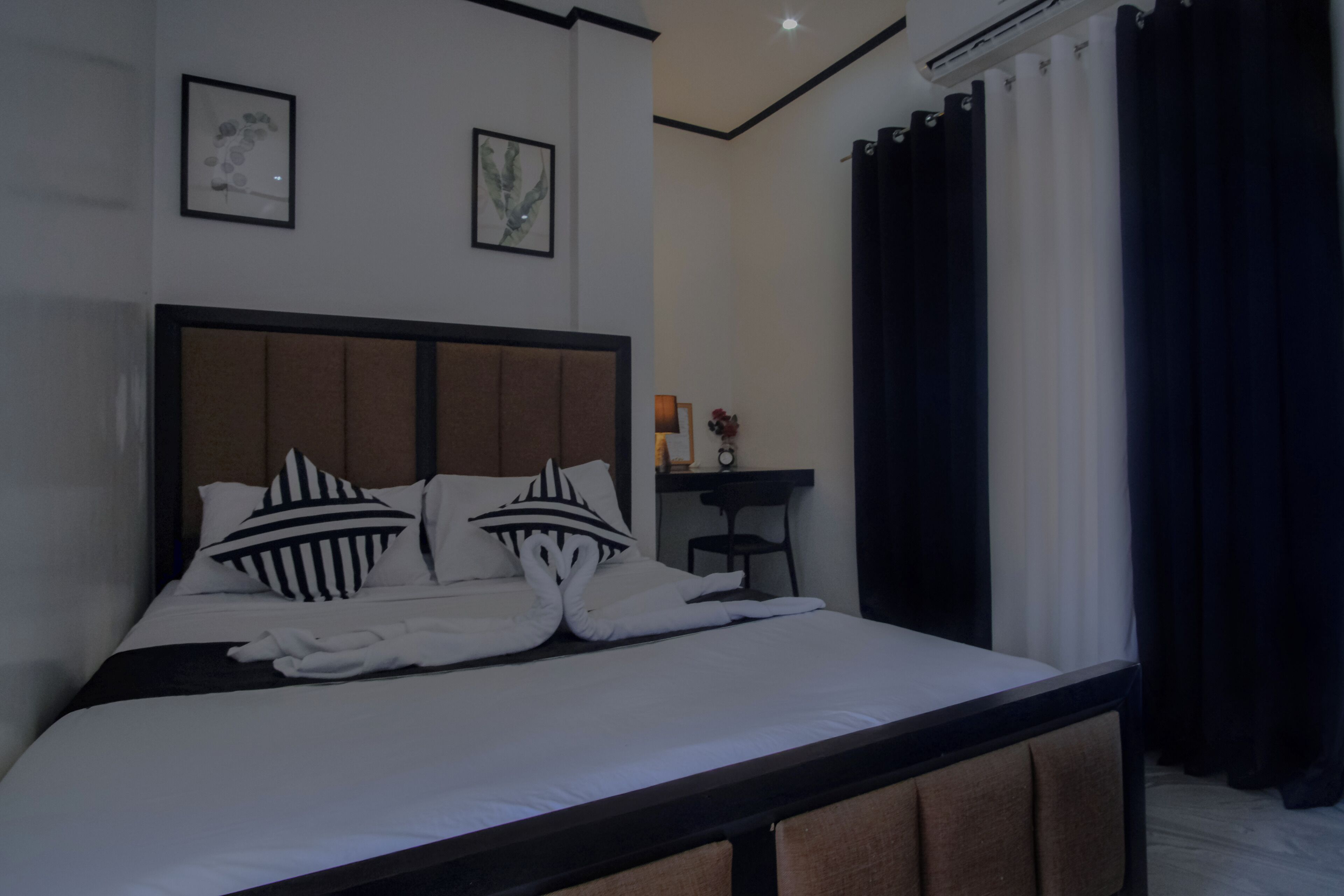 A neatly made bed with striped pillows, a bedside table with a lamp, and a framed picture on the wall.