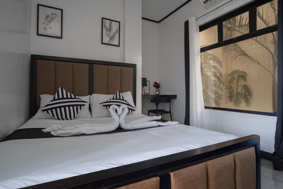 Una cama bien hecha con cabecera, ropa de cama blanca y dos almohadones decorativos.