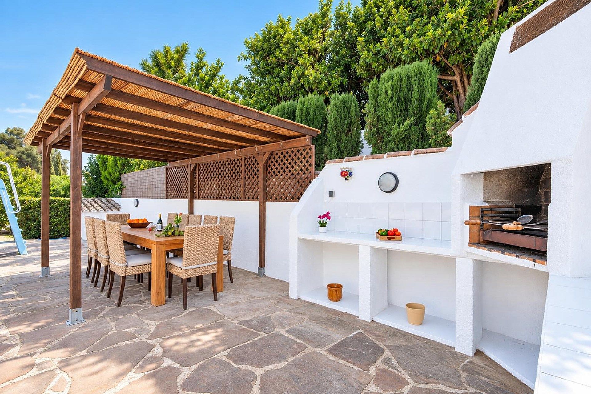 An outdoor patio with a wooden pergola, stone flooring, and a built-in barbecue area.