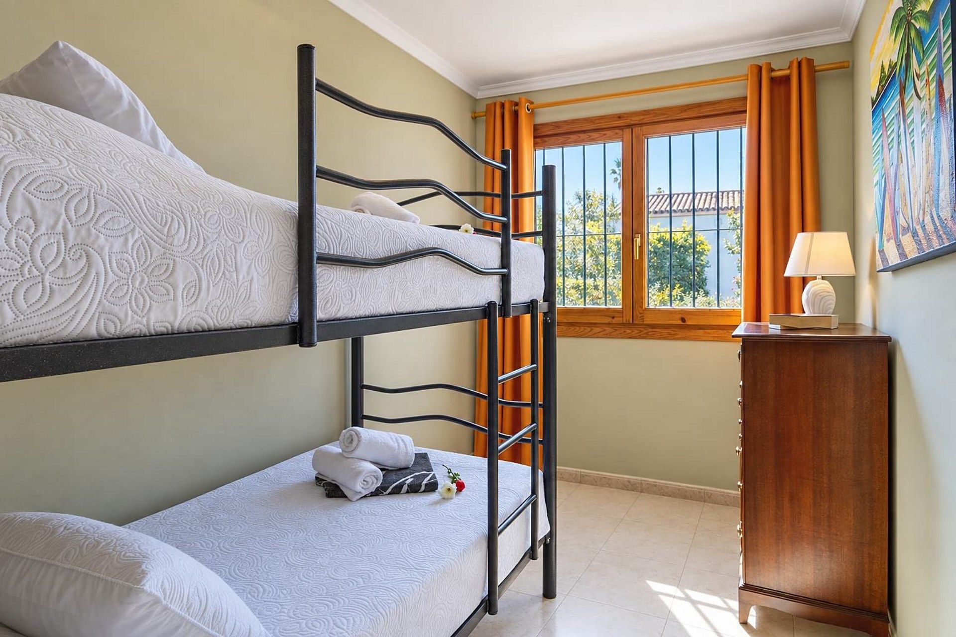 A bunk bed room with a window, a bedside table, and a painting on the wall.