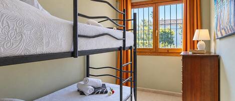 A bunk bed room with a window, a bedside table, and a painting on the wall.