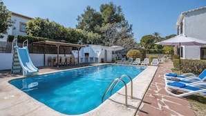 A swimming pool with a slide, lounge chairs, and umbrellas.