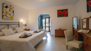A bedroom with a large bed, a wooden dresser, a desk with a mirror, and artwork on the walls.