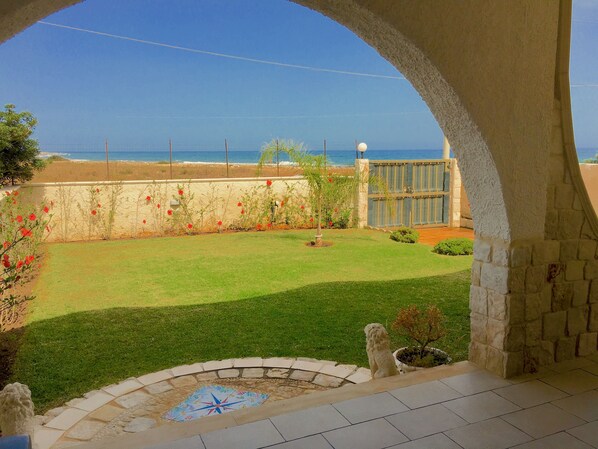 A patio area with a view of the ocean, a stone wall, and a small garden with a decorative tile.