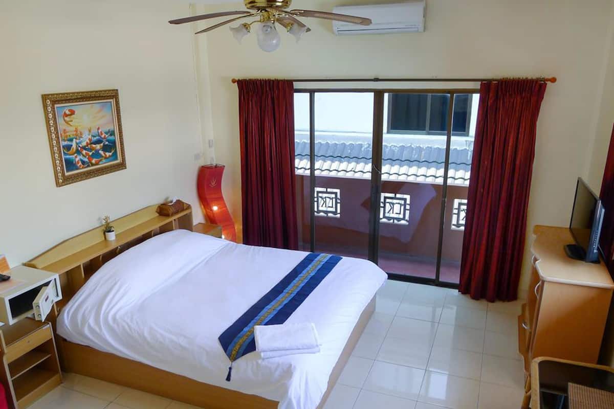 A hotel room with a bed, a desk, a chair, a TV, a ceiling fan, and a balcony with red curtains.