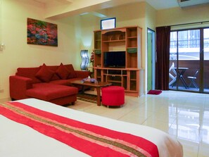 Une chambre d’hôtel avec un grand lit, un canapé rouge, un meuble pour la télévision et un balcon avec une table et des chaises.