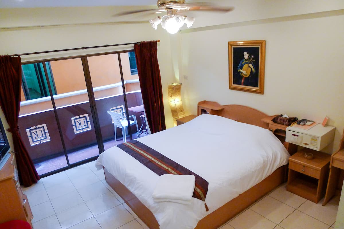A hotel room with a large bed, a desk with a lamp, a chair, and a view of the outside through a sliding door.