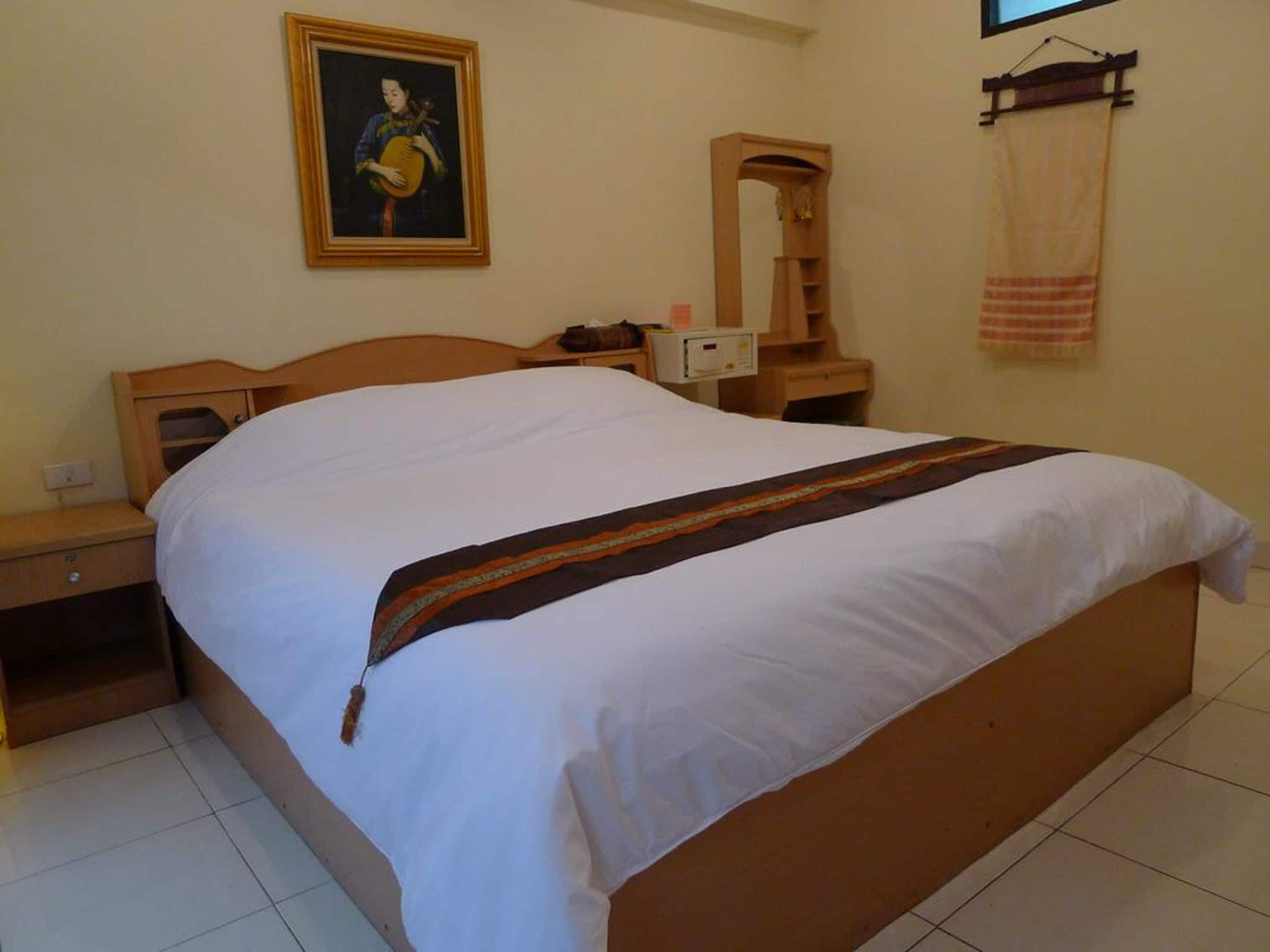 A hotel room with a large bed, a nightstand, a dresser, a mirror, and a painting on the wall.