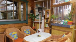 A cozy corner with wicker furniture, a table, and a bookshelf with books and decorative items. - Wockninsee - Finnish log house & round log house (Ückeritz)