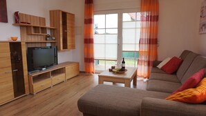 Un salon avec un téléviseur, des meubles en bois, un canapé et une table sur laquelle se trouvent une bouteille et des verres.