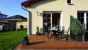 Une terrasse avec une table et des chaises, un pot de fleurs et une clôture verte.