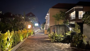 A nighttime street with a paved walkway, buildings on either side, and illuminated plants. - Lovecho Villa & Room Unit Canggu (Canggu)