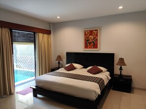 A bedroom with a bed, two bedside tables, a nightstand, a window with curtains, and a painting on the wall. - Lovecho Villa & Room Unit Canggu (Canggu)