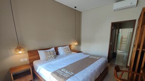 A bedroom with a wooden bed, bedside tables, a chair, and a hanging light fixture. - Lovecho Villa & Room Unit Canggu (Canggu)