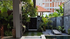 A modern outdoor pool area with a wooden deck, a stone pathway, and lush greenery. - Lovecho Villa & Room Unit Canggu (Canggu)