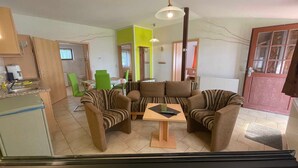 Ein Wohnzimmer mit einer Sofagarnitur, einem Esstisch und einer Küchenzeile mit Kühlschrank und Spüle.