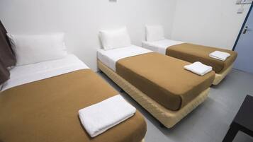 A hotel room with three beds, each with a white pillow and a brown bedspread. There are white towels on the beds.